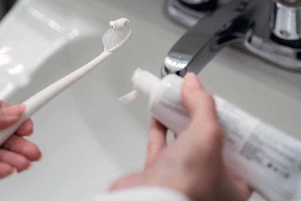 Someone putting toothpaste onto a toothbrush over a sink