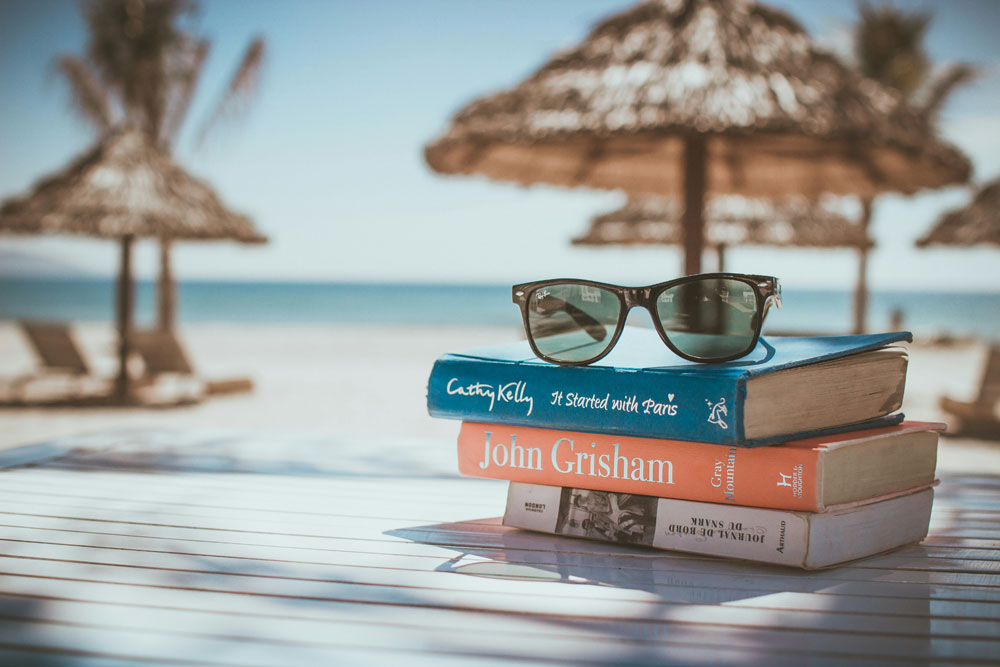 A selection of books with a pair of sunglasses, on the beach